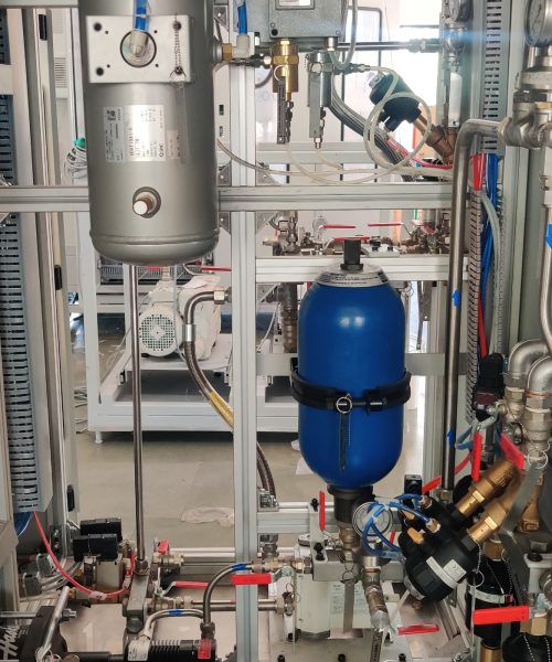 A machine with a silver tank, a blue tank, and a complex network of pipes, valves, and gauges on a metal frame.